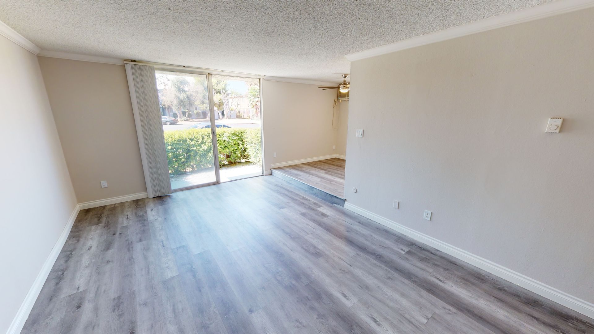 Empty living room with gray wood-look flooring, sliding glass door, and neutral-colored walls.