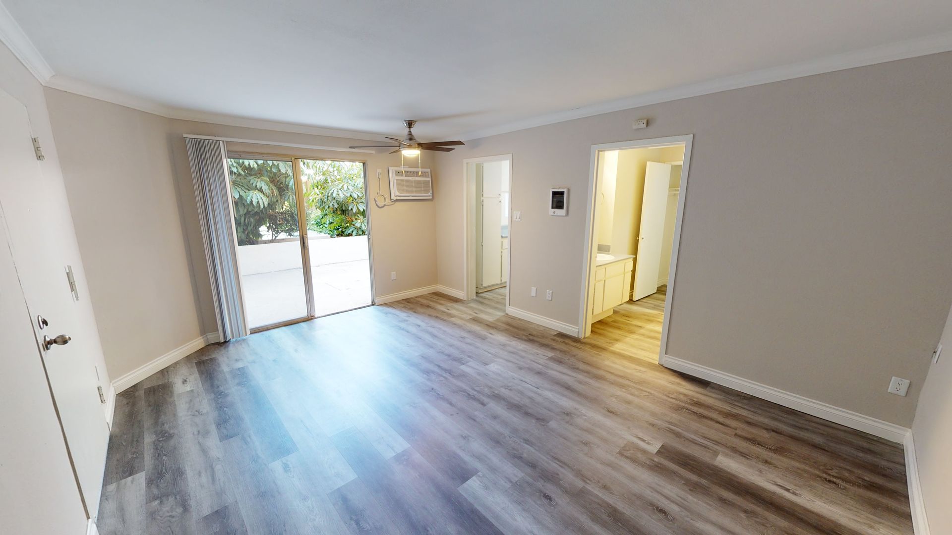 Interior apartment view with gray wood flooring, a sliding door to a patio, and a doorway to a bathroom.