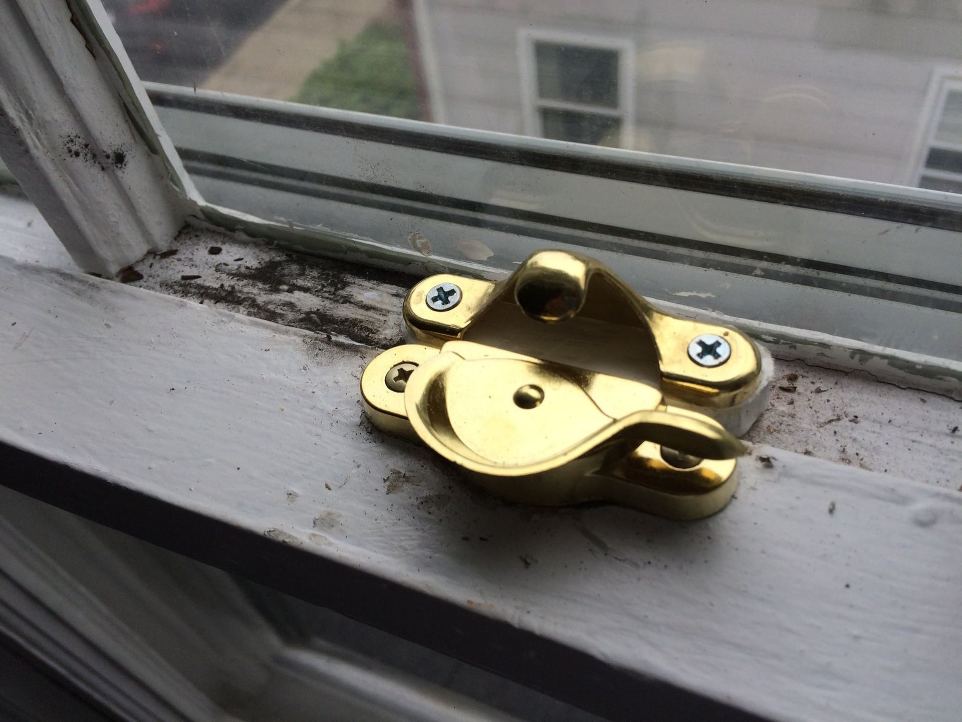 A brass window lock is sitting on a window sill.
