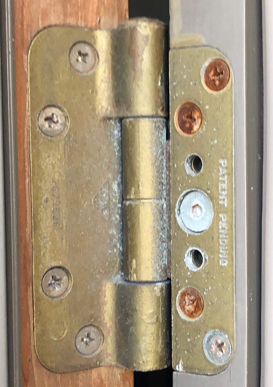 A close up of a brass door hinge on a wooden door.