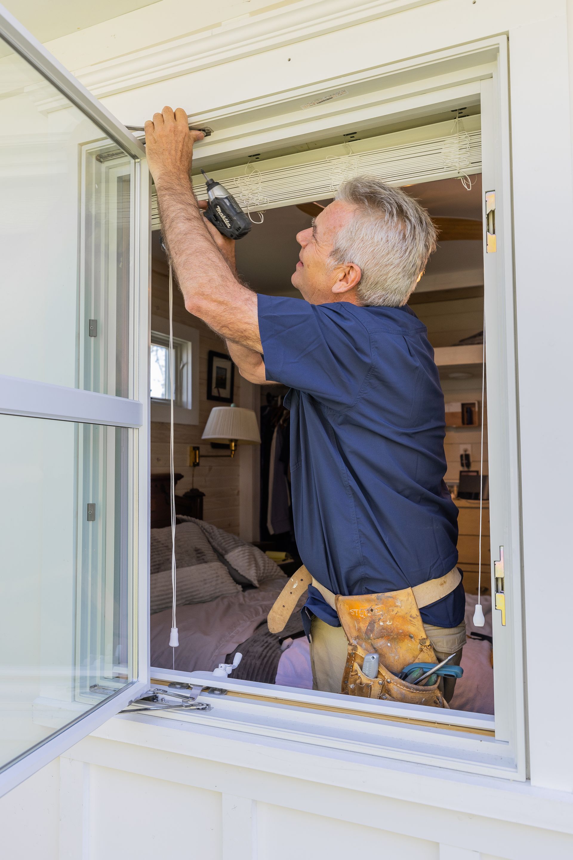 A man is working on a window with a drill.