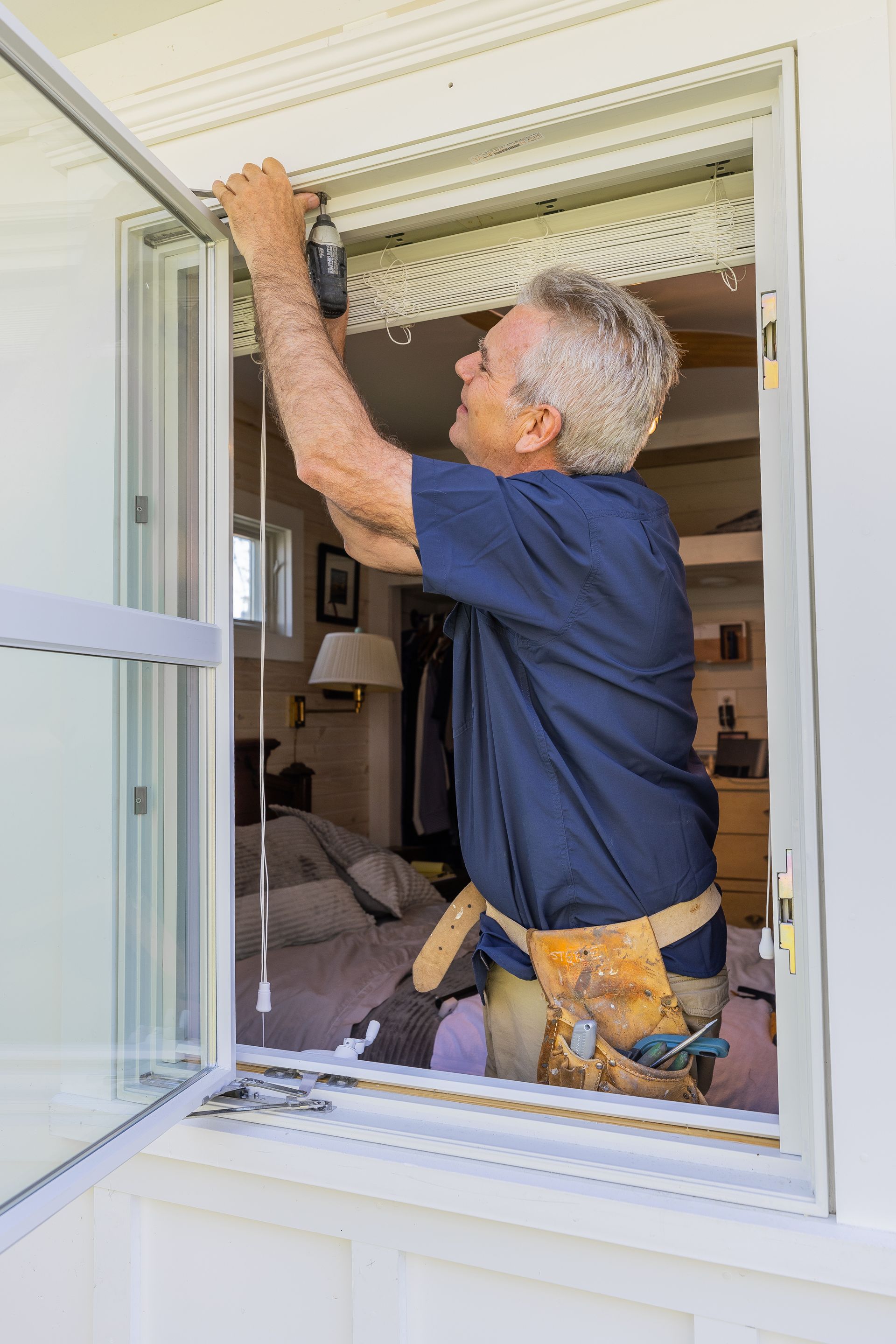 A man is working on a window in a living room.