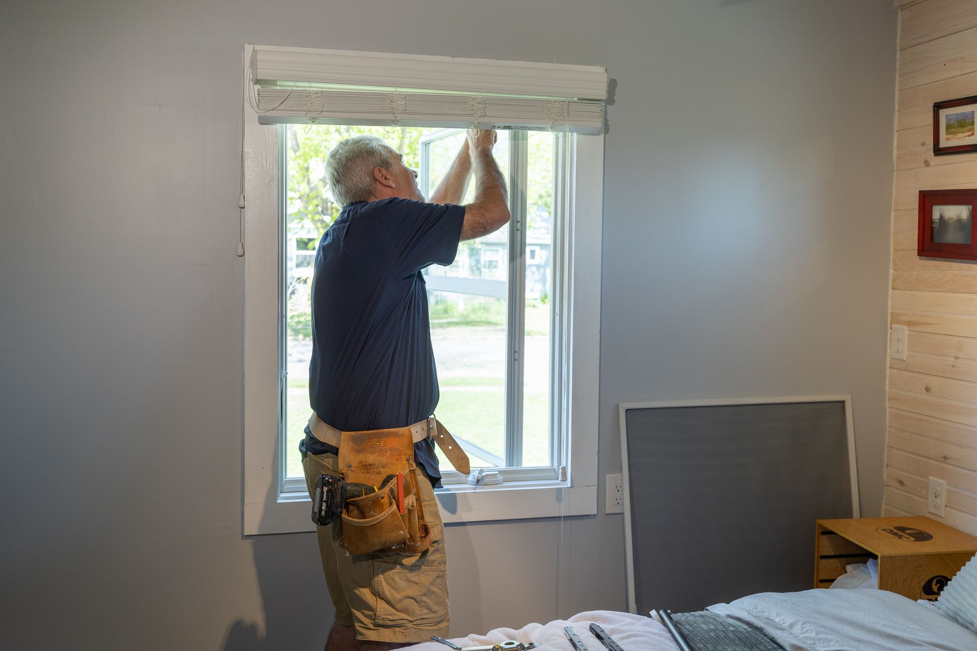 A man is installing a window in a bedroom.