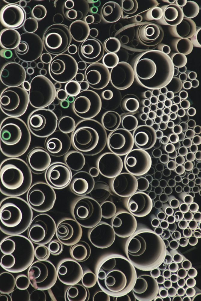 Una densa colección monocromática de tubos de PVC y cartón apilados de varios tamaños, que crean un patrón circular.