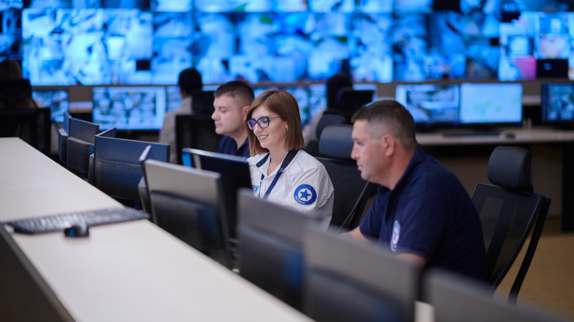 A group of people are sitting in front of computer monitors in a control room.