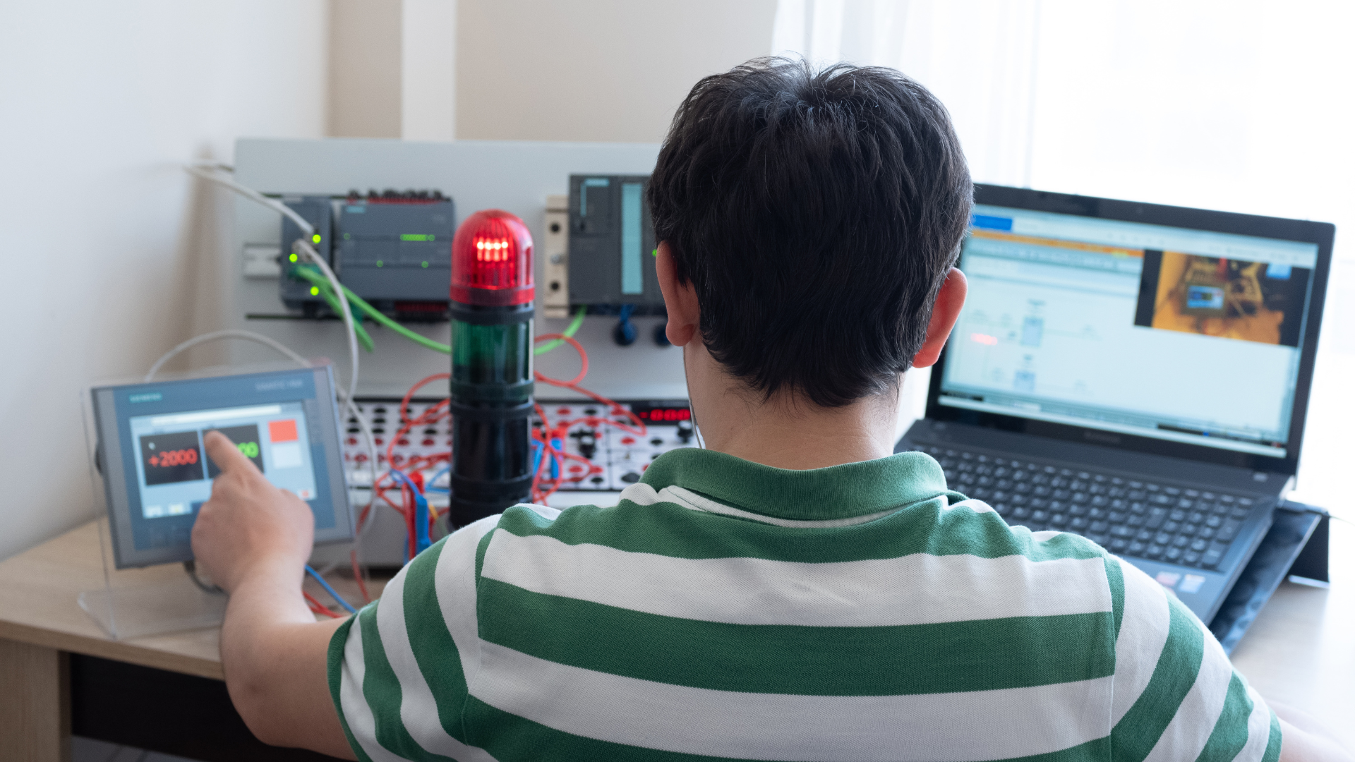 A man in a green and white striped shirt is sitting in front of a laptop computer.