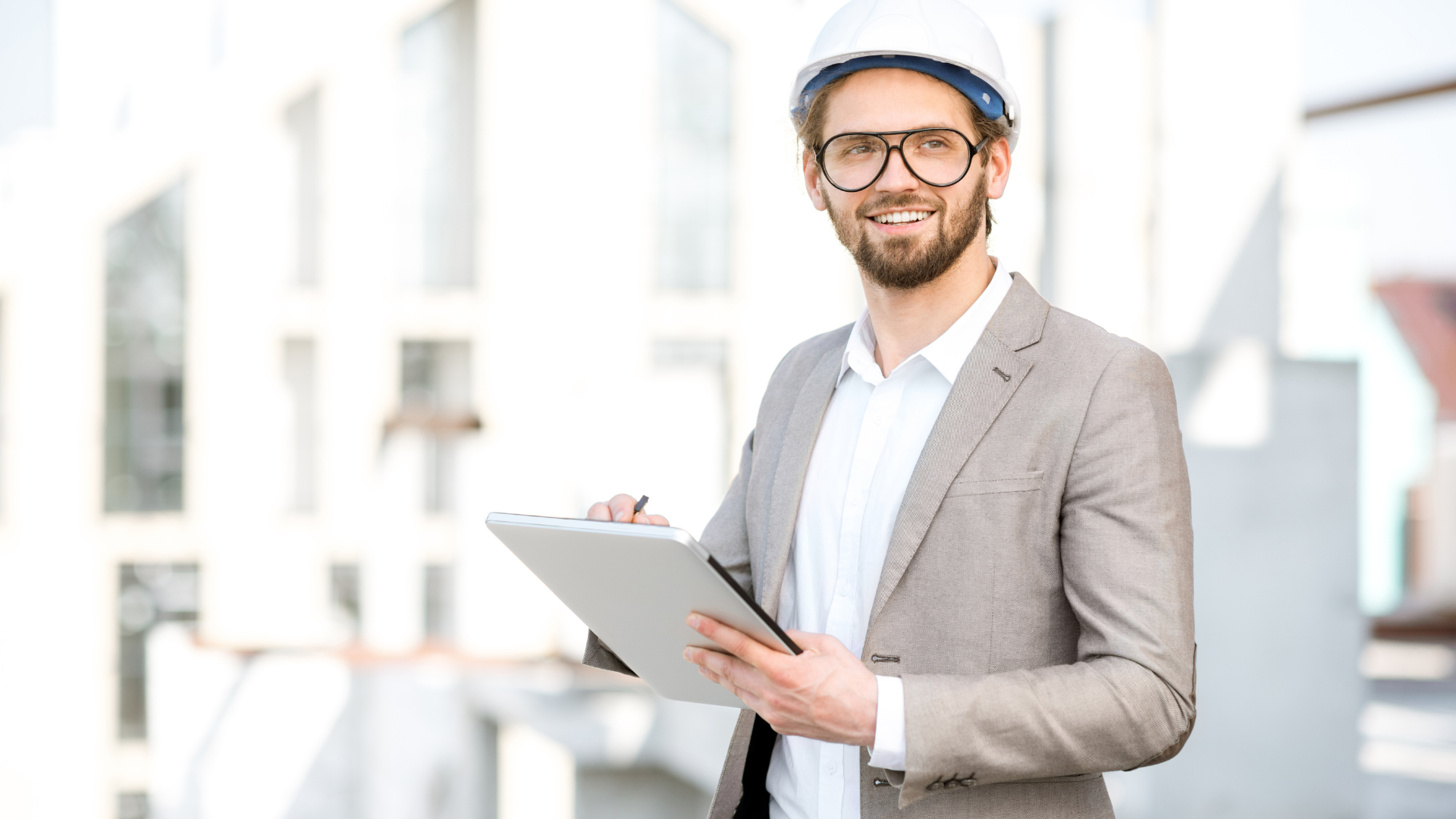 A man in a suit and hard hat is holding a clipboard.