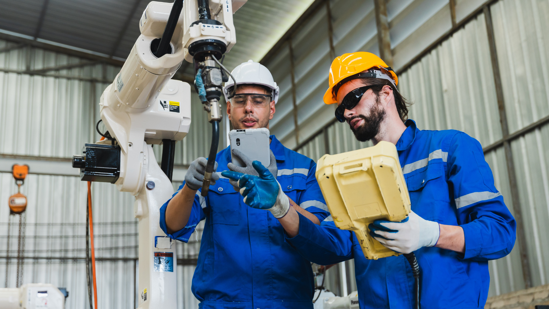 Two engineers are working on a robotic arm in a factory.