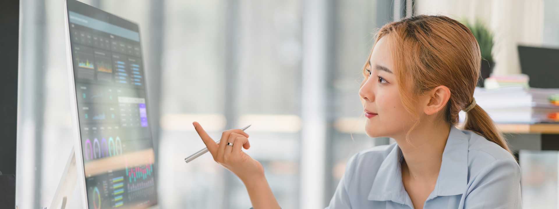 A woman is pointing at a computer screen while sitting at a desk.