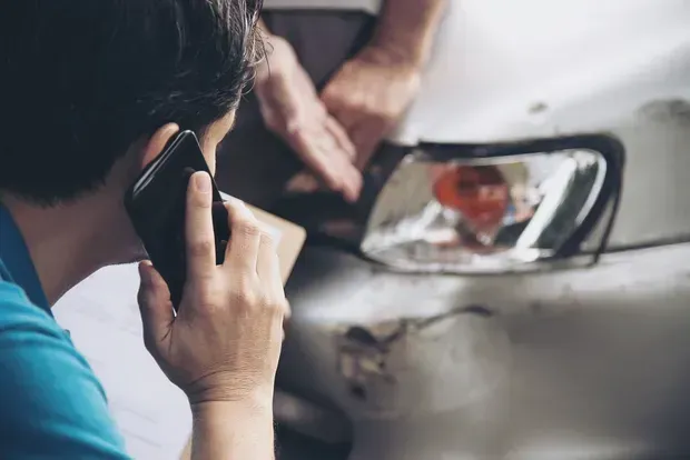 Man in protective gear sanding a car door in a body shop.
