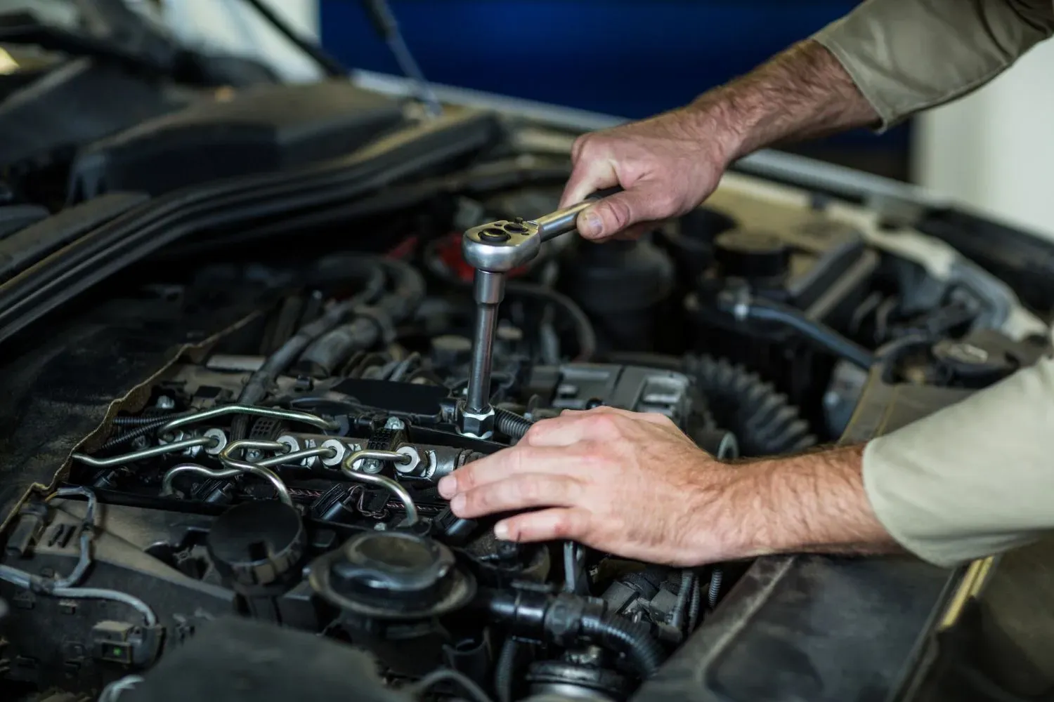 Mechanic's hands using a wrench to work on a car engine in a garage.