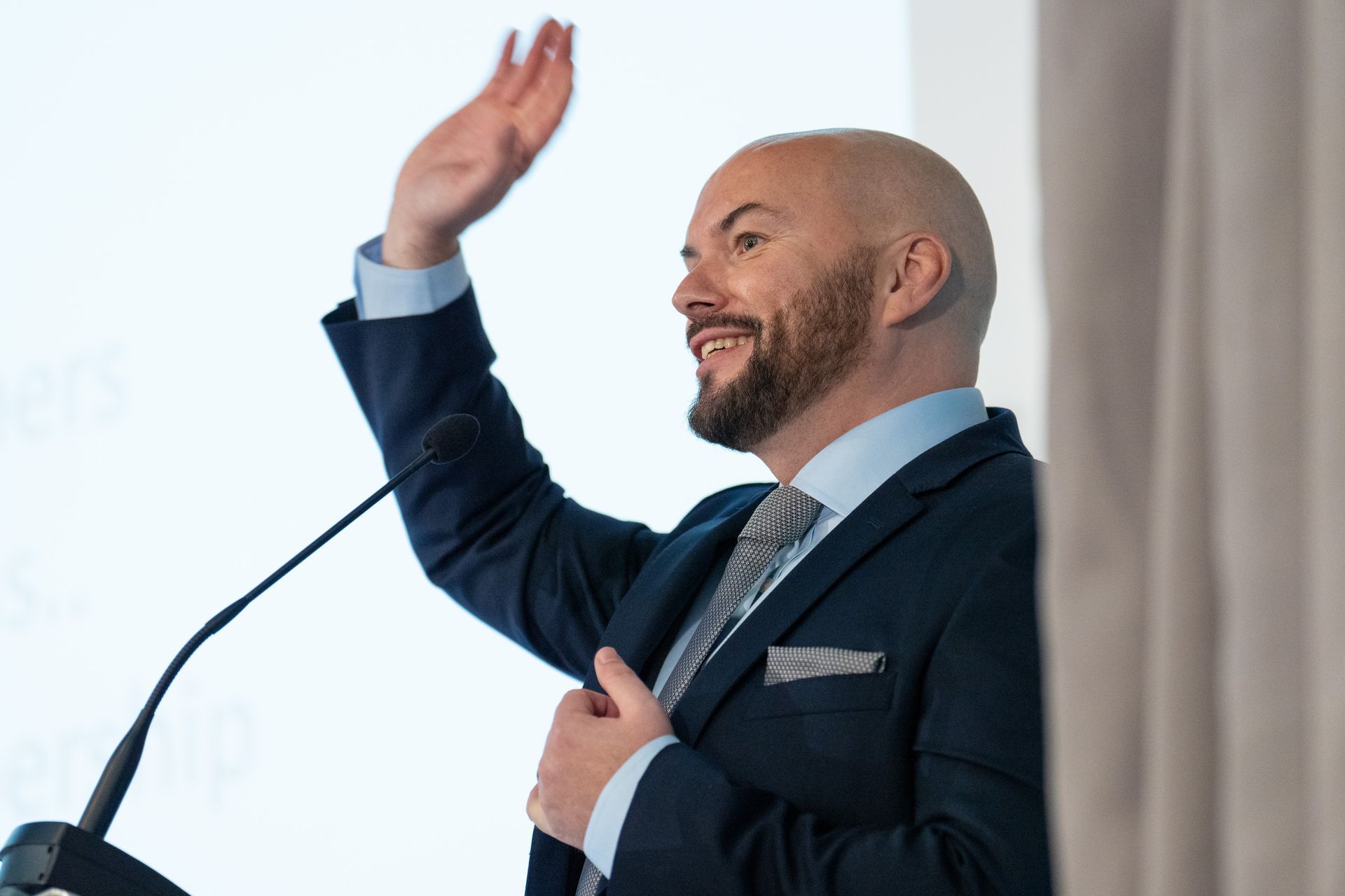 A man in a suit and tie is giving a speech in front of a microphone.
