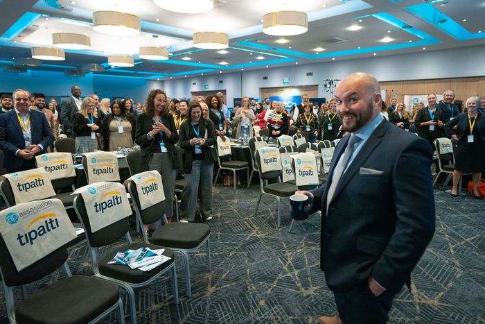 A man in a suit is standing in front of a crowd of people in a conference room.