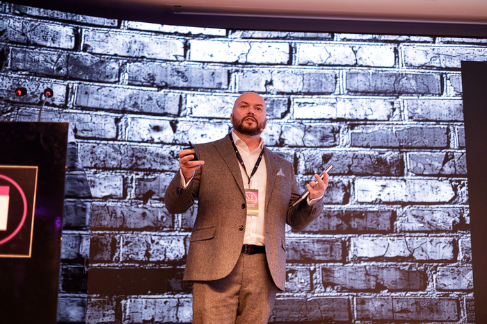 A man in a suit is giving a presentation in front of a brick wall.