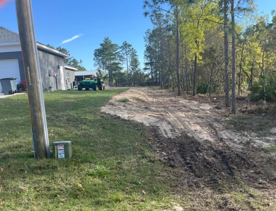 Dirt road and grassy lawn next to a house with a green tractor. Power pole in the foreground.