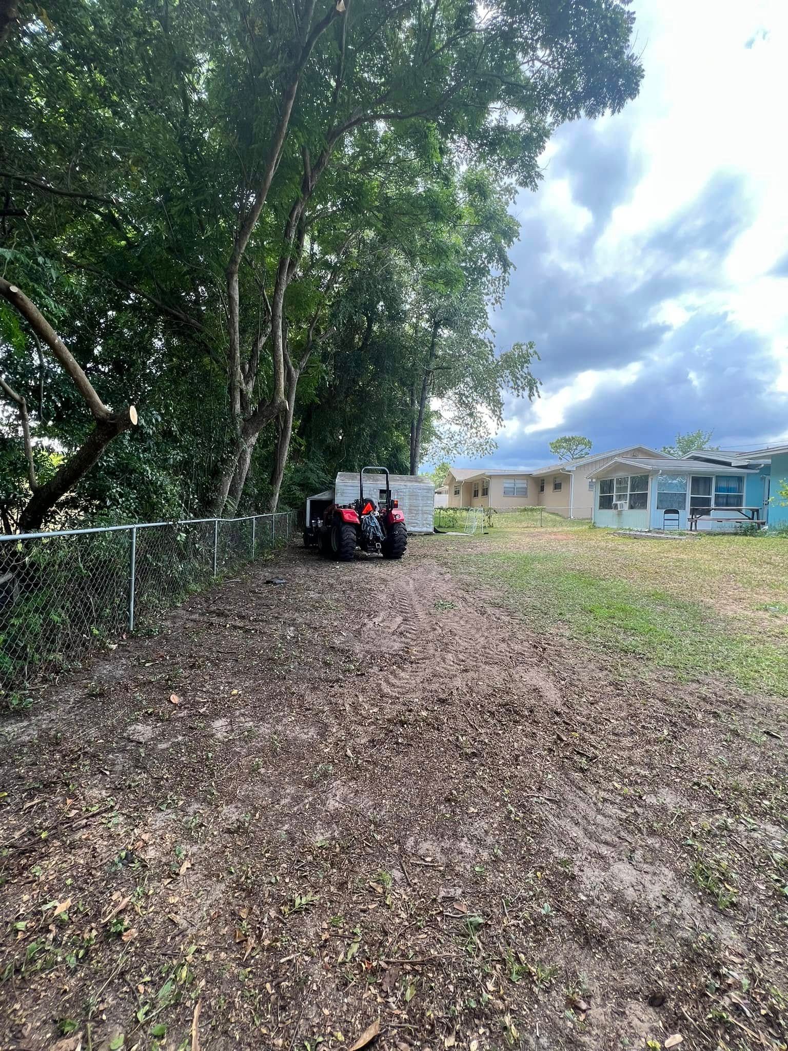 Muddy dirt path leading to a red ATV near trees and a house on a cloudy day.