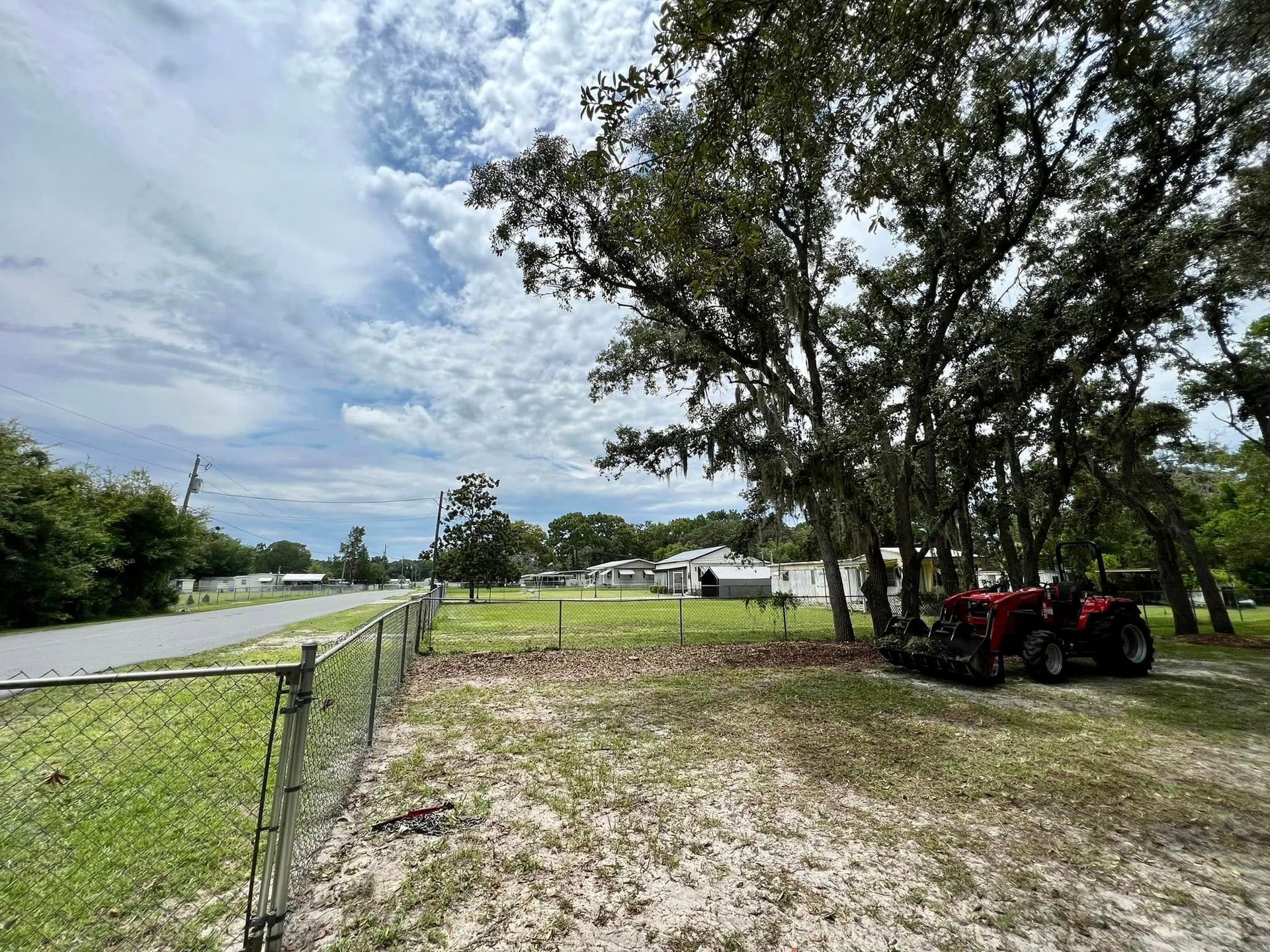 A rural property with a tractor near trees and a road under a cloudy sky.