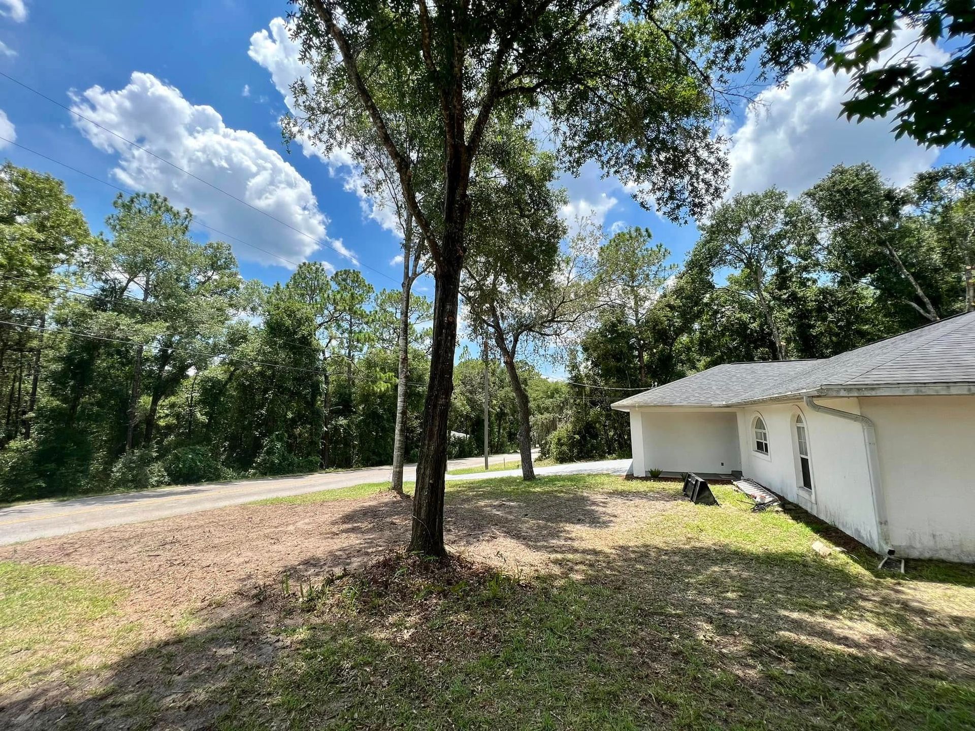 A house with a white exterior, trees, and a partly cloudy blue sky.