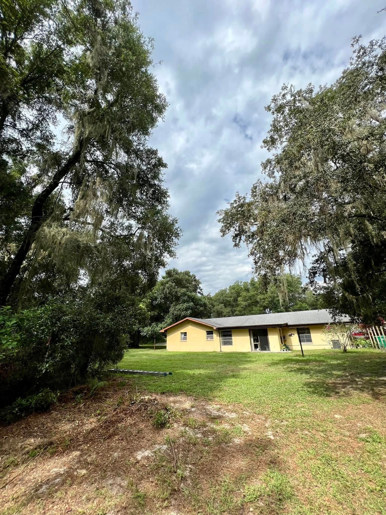 Yellow house nestled in a grassy area, flanked by trees with cloudy sky above.