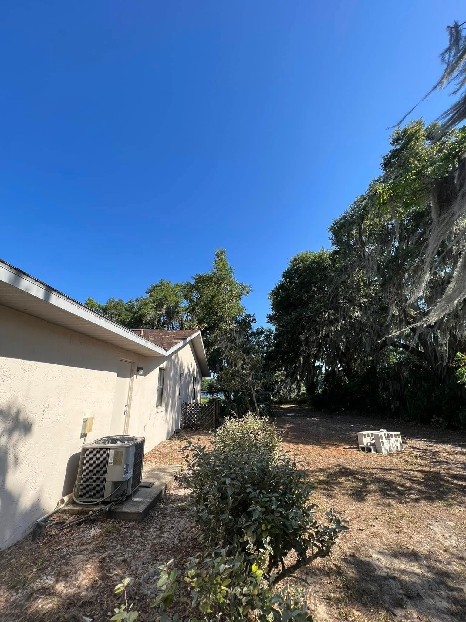 Backyard with a stucco house, air conditioning unit, trees, and bright blue sky.