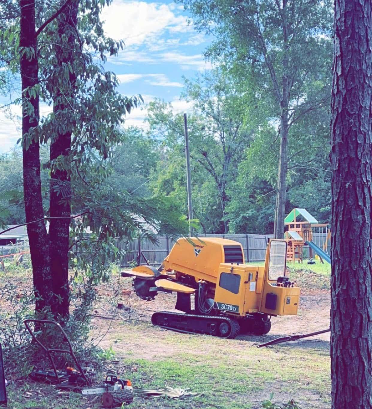 Yellow stump grinder removing a tree stump in a yard, playground in the background.