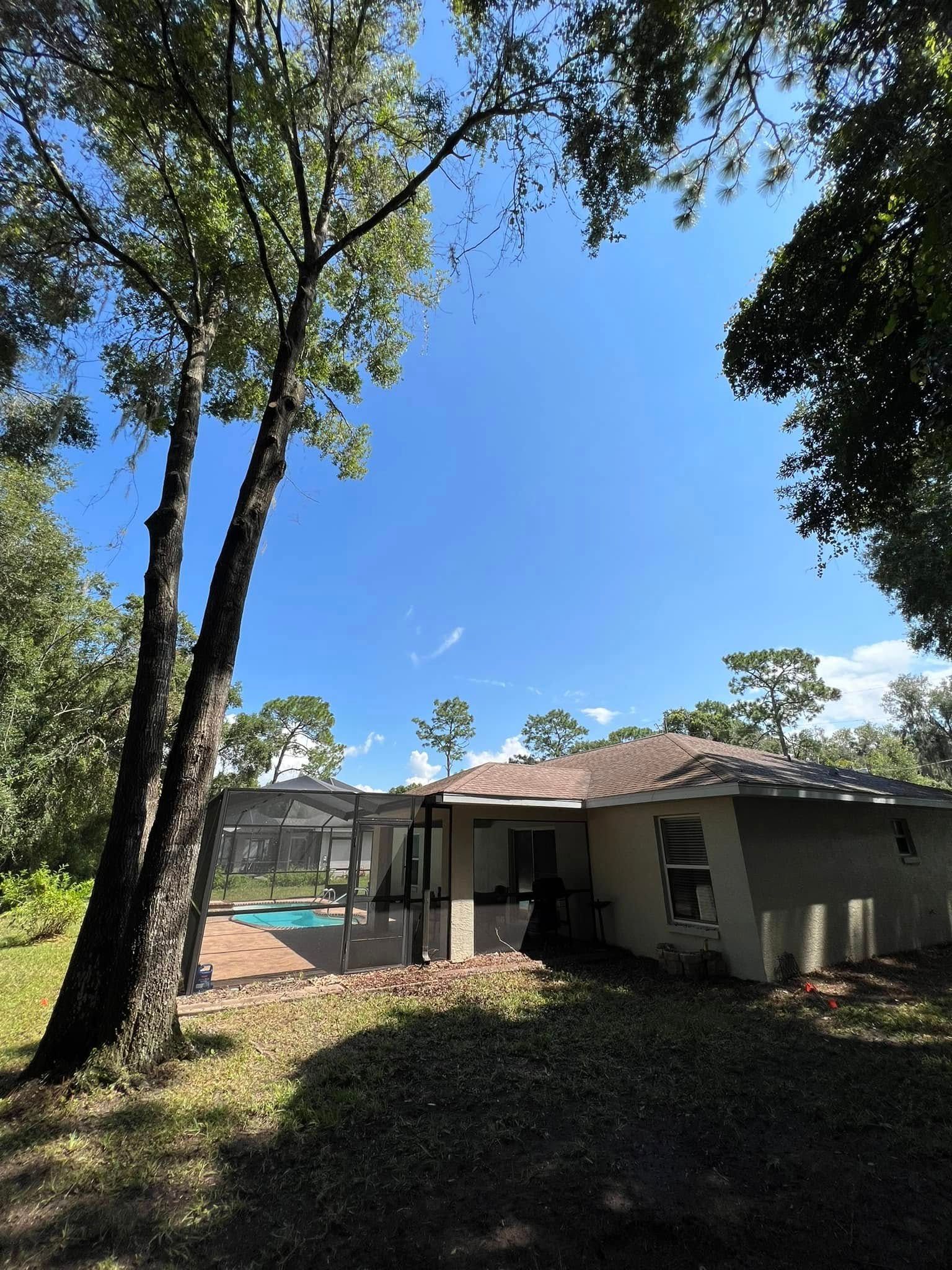 Backyard view of a house with a screened-in pool, trees, and blue sky.