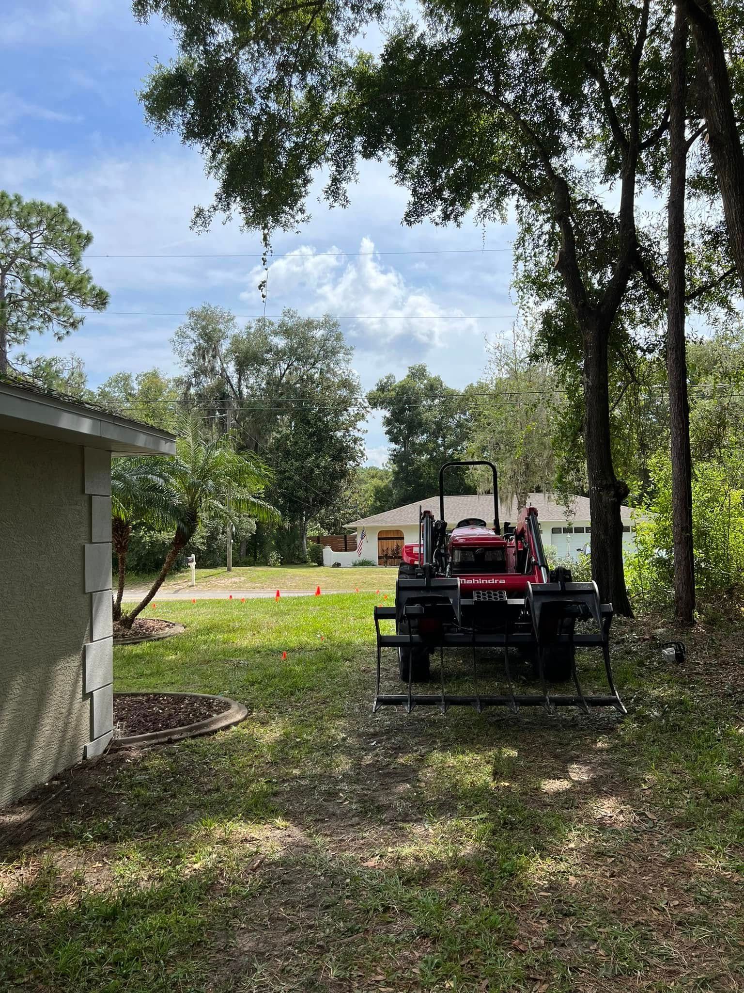 A red tractor with a front-end loader sits in a grassy yard. A house and trees are in the background.