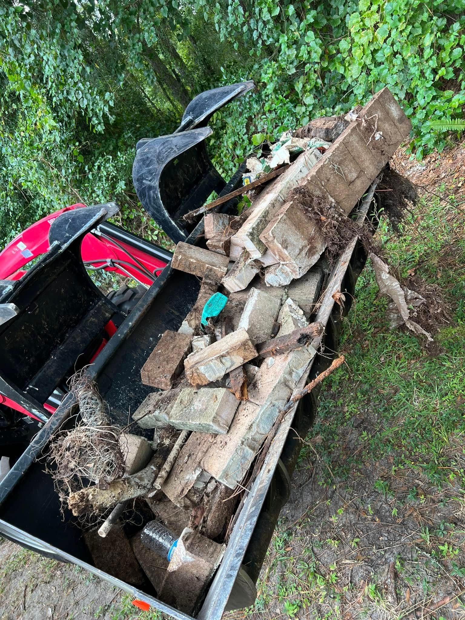 Red tractor bucket filled with debris and broken wood outdoors.