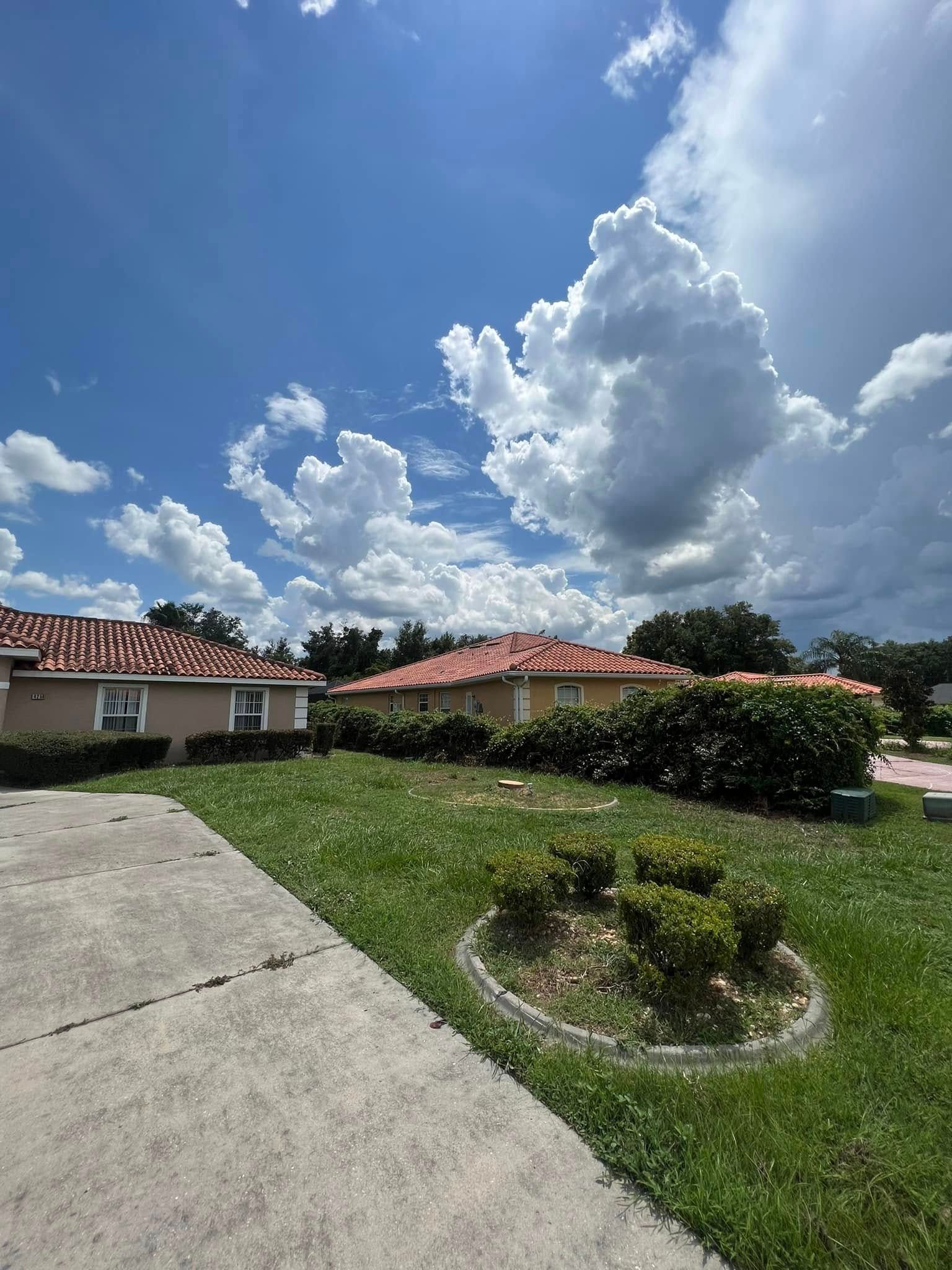 Residential houses with red-tiled roofs under a blue sky with fluffy white clouds, and a green lawn.