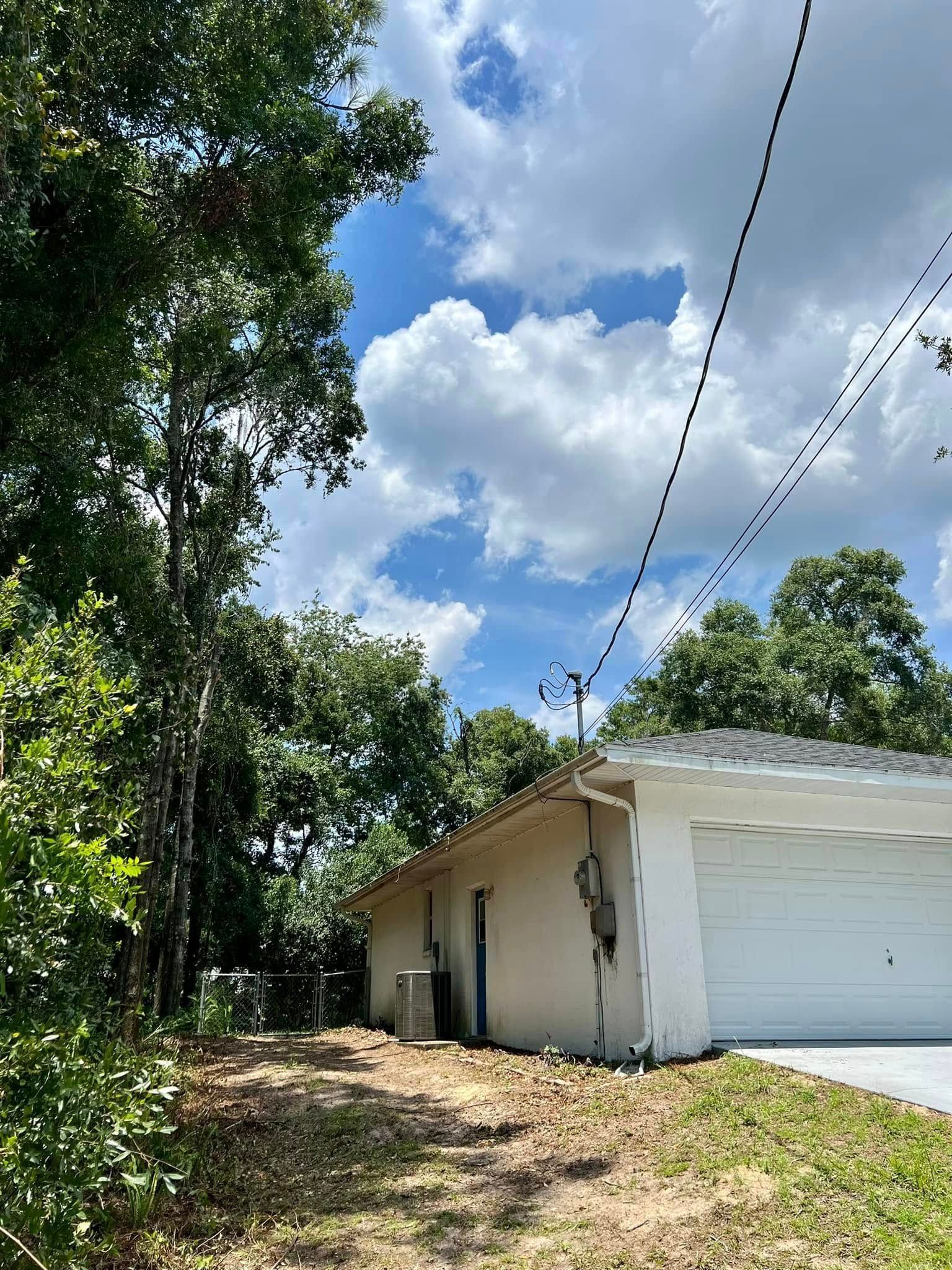 A residential house exterior with trees, driveway, and power lines against a partly cloudy sky.