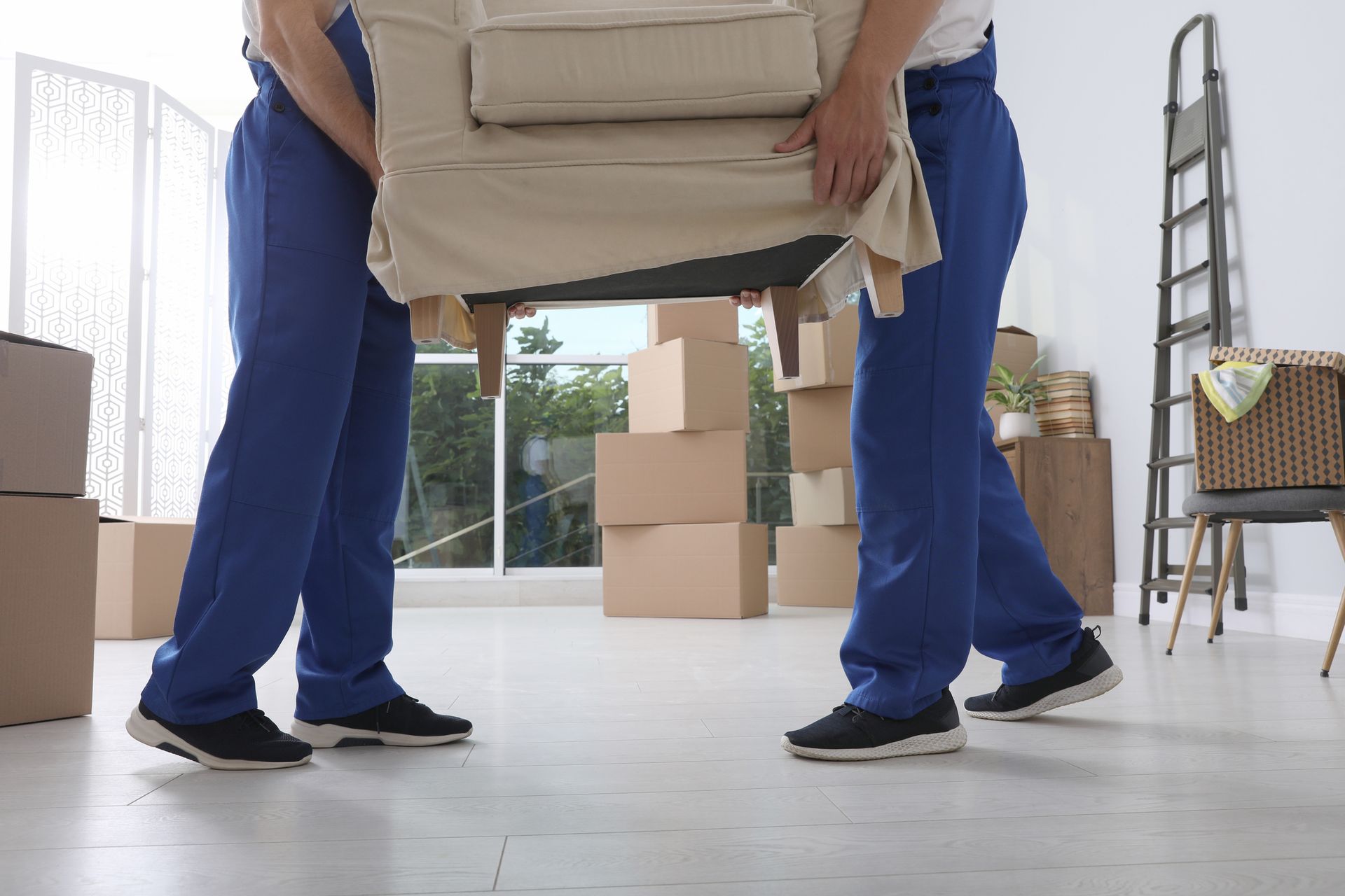 Two men are carrying a couch in a living room.
