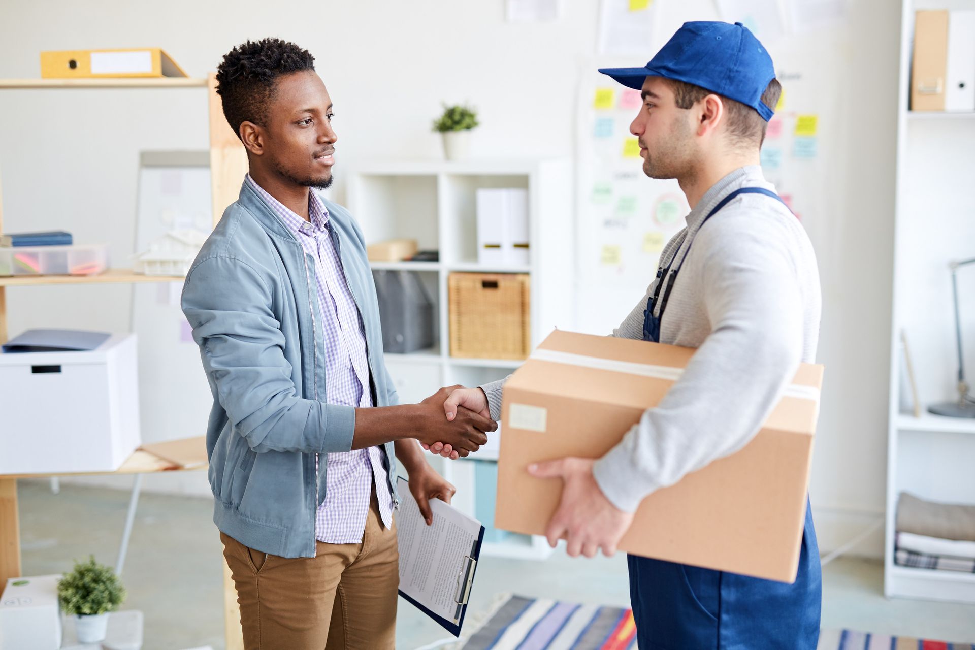 A man is shaking hands with a delivery man who is holding a box.