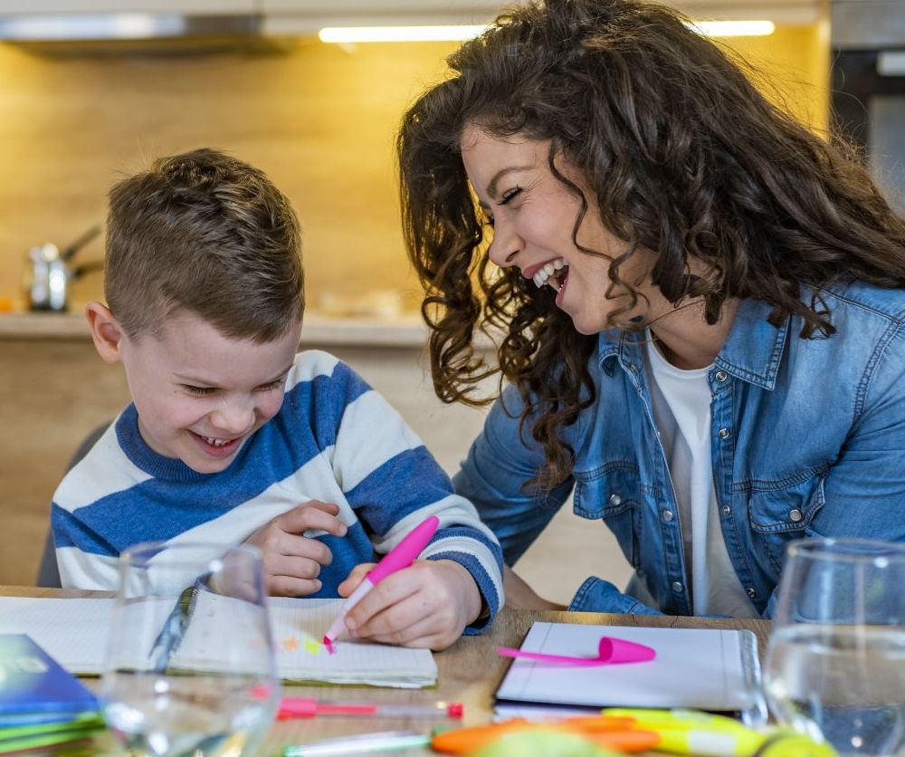 A woman is helping a young boy with his homework at a table.