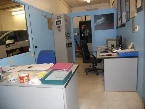 Interno di un ufficio con pareti blu, due scrivanie e una sedia da ufficio nera, visti attraverso una parete in vetro.