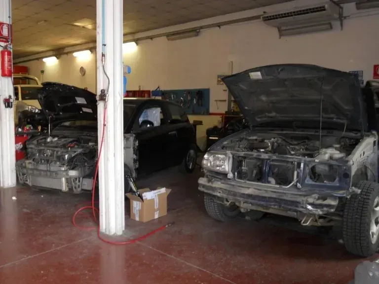 Due auto con il cofano aperto in riparazione all'interno di un'officina meccanica ben illuminata e con il pavimento rosso.