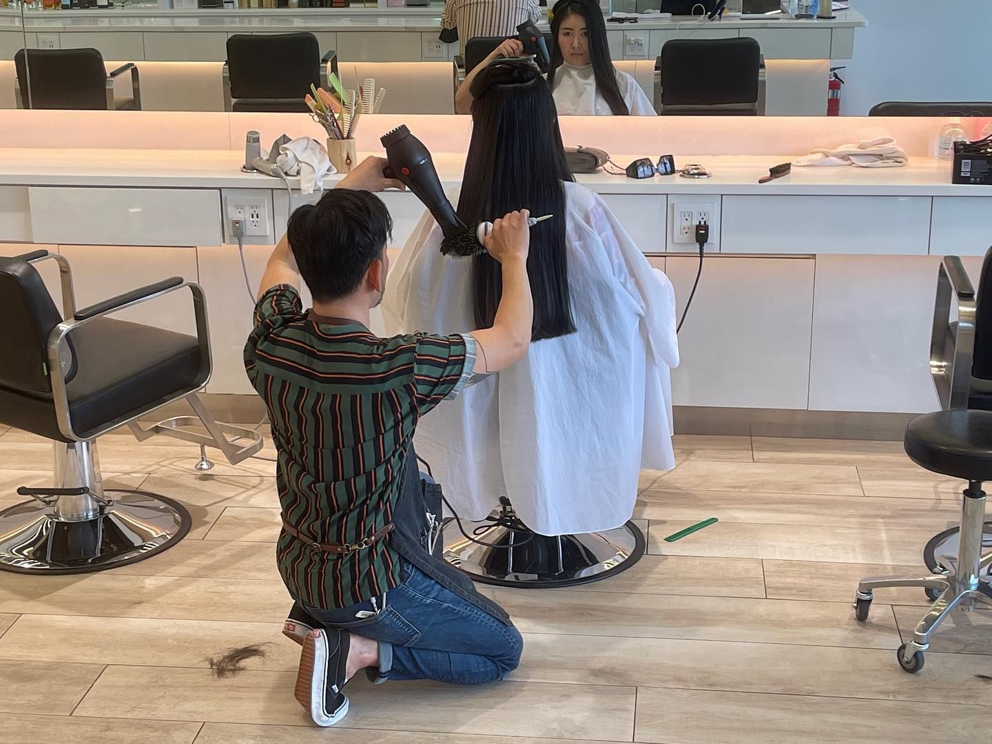 A man is kneeling down in a hair salon cutting a woman 's hair.