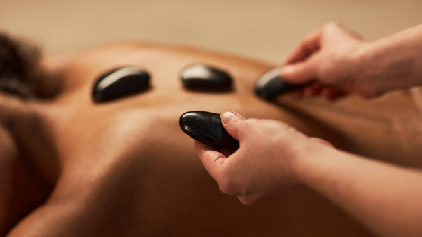 Hands placing hot stones on a person's back during a massage, in a spa setting.