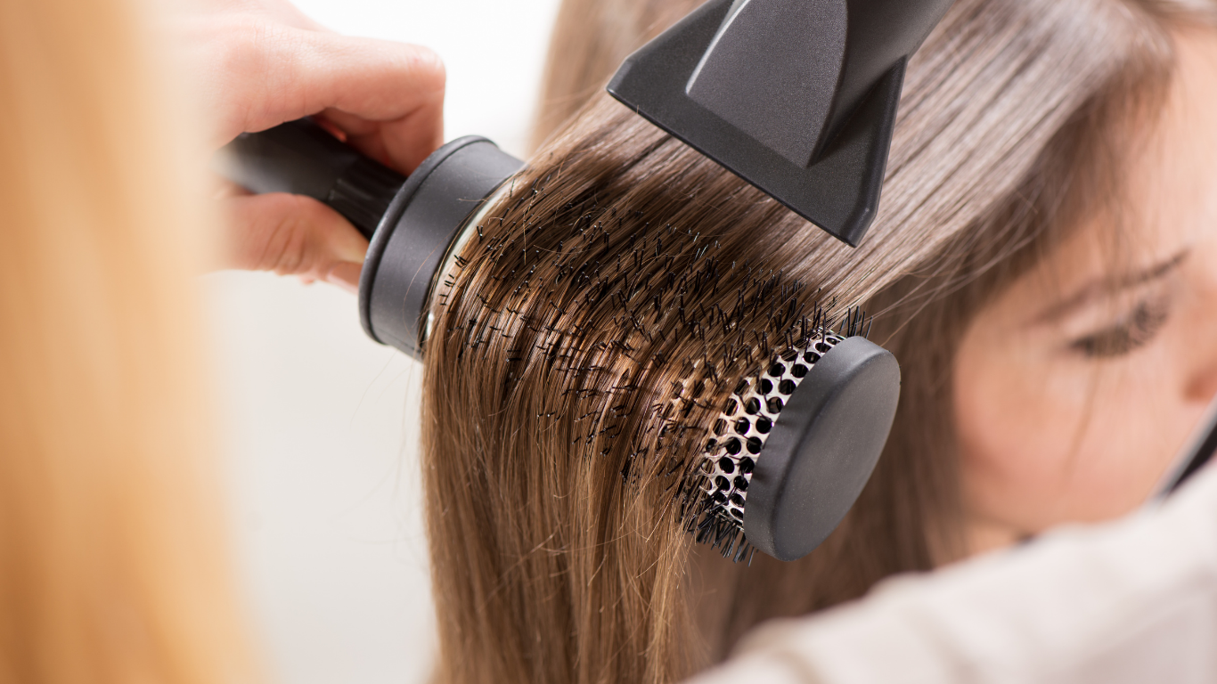 A woman is getting her hair blow dried with a round brush.