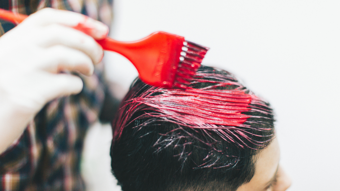 A man is getting his hair dyed red by a hairdresser.