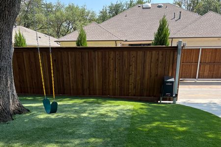 A swing is hanging from a tree in front of a wooden fence.