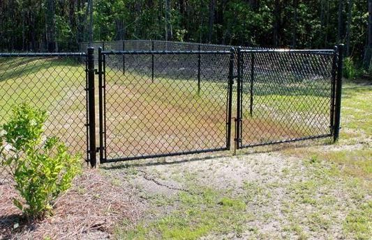 A chain link fence with a gate in the middle of a grassy field.