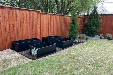 A backyard with a wooden fence and planters in the grass.