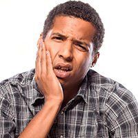 A man in a plaid shirt is holding his face in pain.