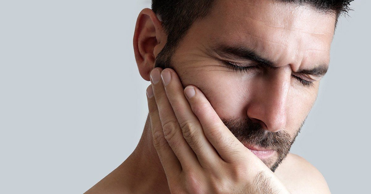 bearded caucasian male experiencing painful tooth abscess symptoms and clutching right cheek