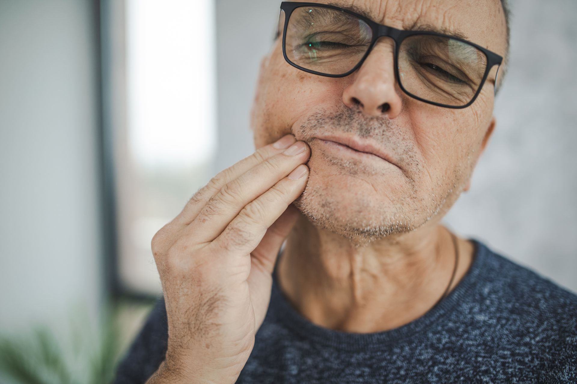 Man with glasses holding cheek, appearing in pain.