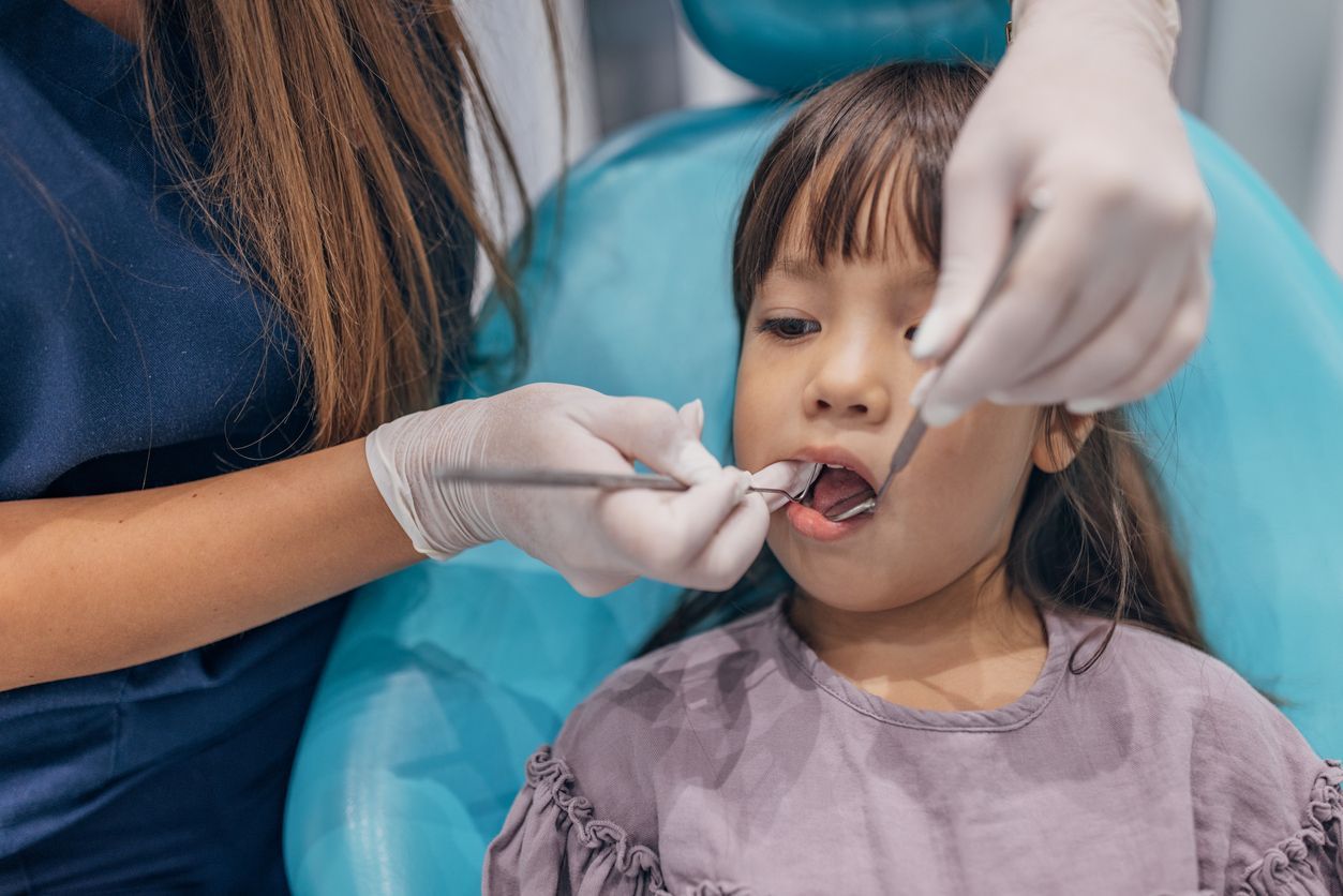 Child in dental chair having teeth examined with tools.
