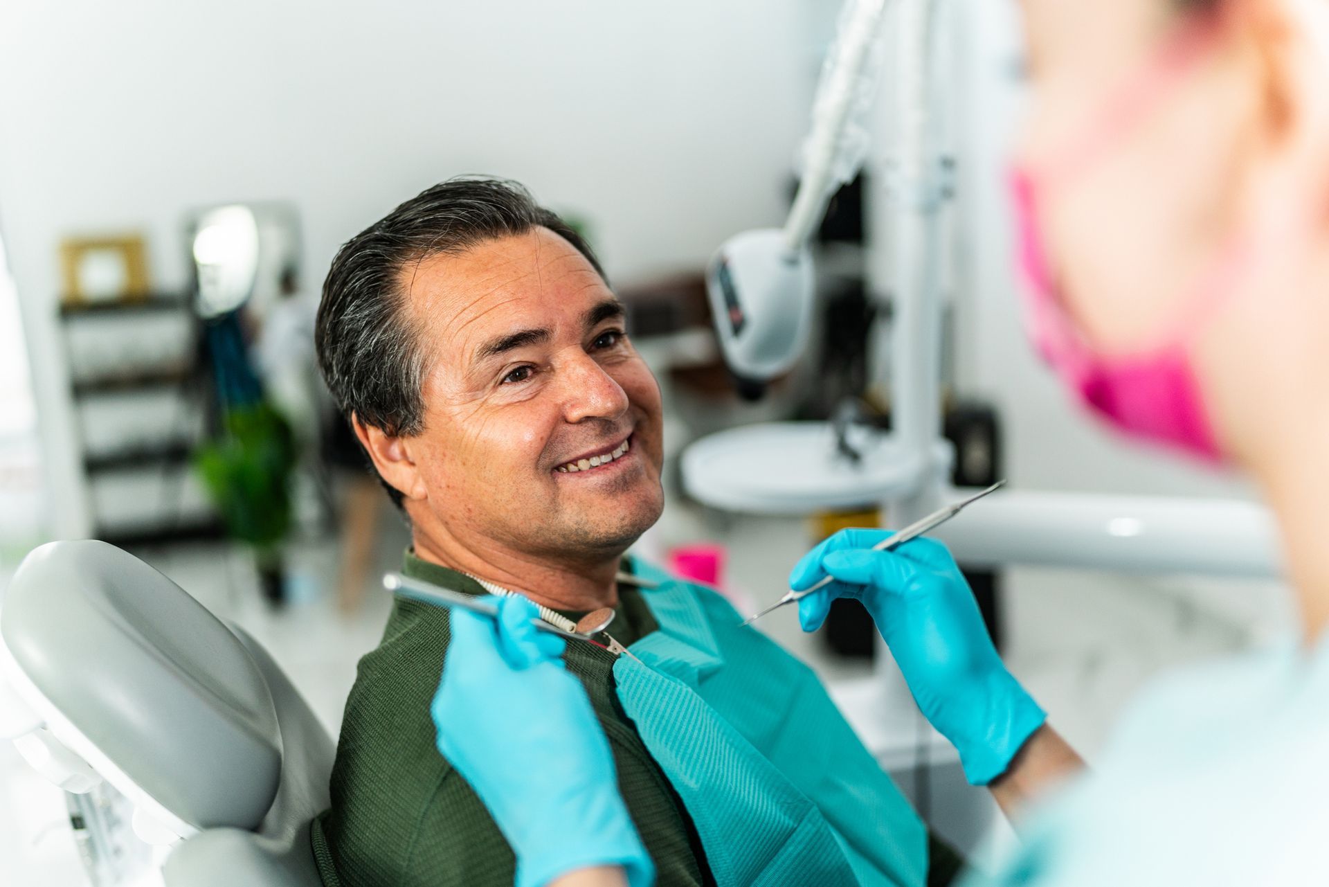 Man smiling at dentist during a dental checkup. Dentist wears gloves and a mask.