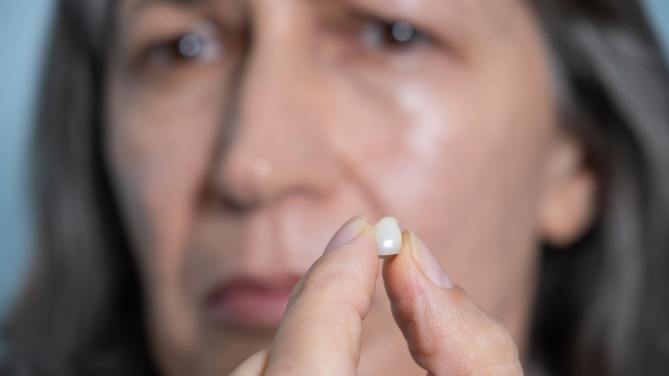Woman holding small pill, looking at it with a doubtful expression.