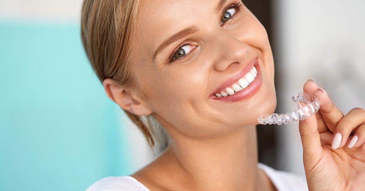 A woman is smiling while holding a clear retainer in her hand.