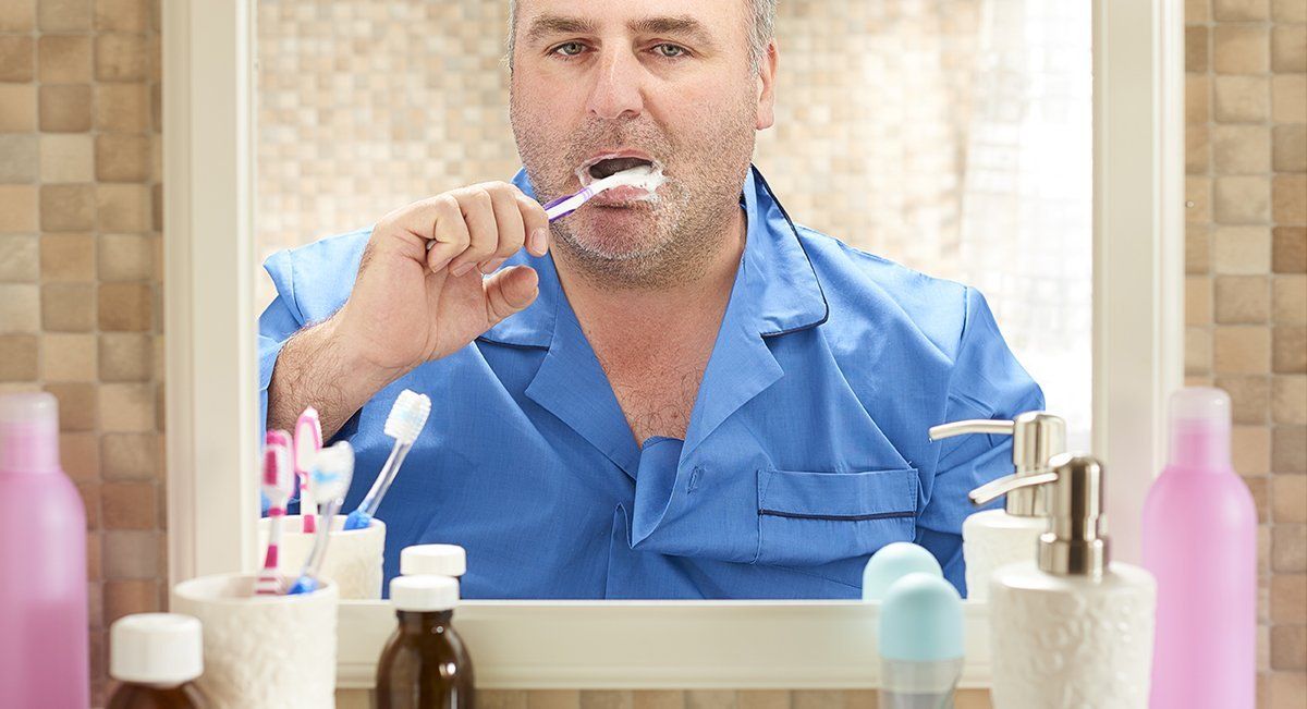 A man is brushing his teeth in front of a bathroom mirror.